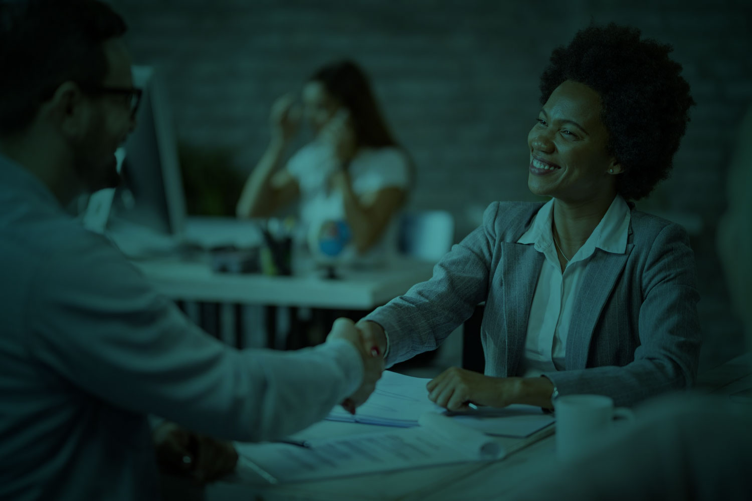 Two professionals shaking hands in a modern, dimly lit office.